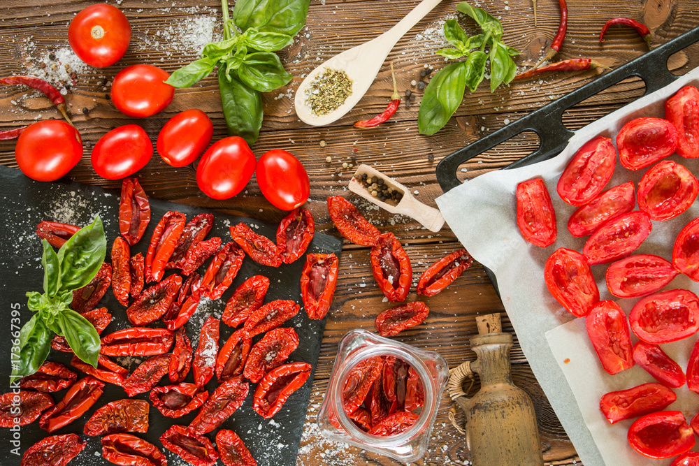 Φωτογραφία tomato fruits, dried tomatoes on pan, sundried  tomatoes in jar, olive oil in clay bottle, basil, herbs in wooden spoon  on a wooden table