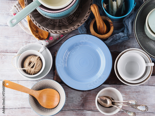 Ceramic and enamel crockery tableware on wooden background. Pastel vintage colors. Blue empty plate for text