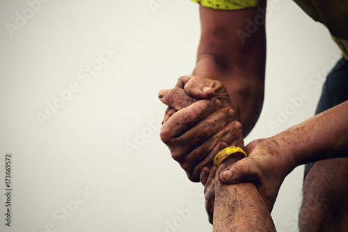 Mud race runners.Couple hold hands,help when overcoming hindrances mud