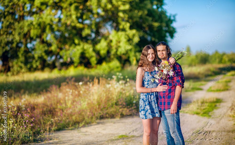 young happy couple walking in the field, the girl in the hands holding a bouquet of wildflowers young happy couple walking in the field, the girl in the hands holding a bouquet of wildflowers