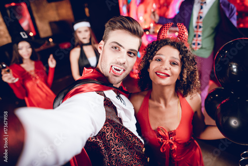 A guy dressed as a vampire and a girl dressed as a demon posing and making selfie on their smartphone