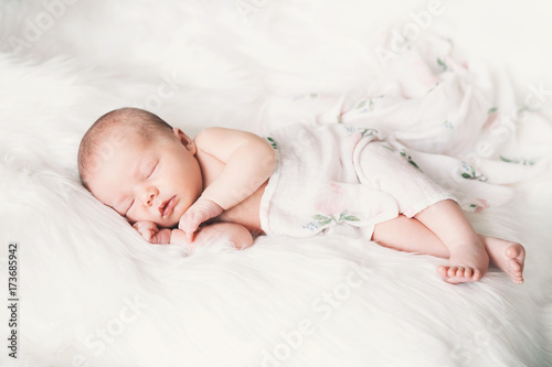 Sleeping newborn baby in a wrap on white blanket.