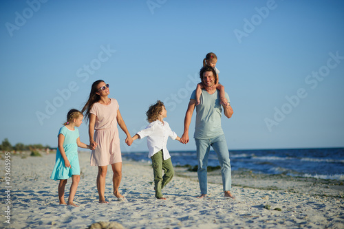 Big happy family walking at the beach. Mom, dad and three children. The blue sky, the sun, fresh sea wind. Pleasure from nature and communication.