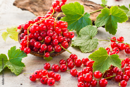 Red currant in a bowl, berries and leaves scattered on a shabby wood