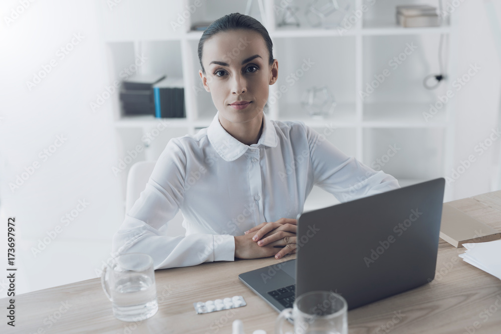 Sick woman sitting at her workplace in the office. Around it lies a pile of pills