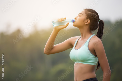 Asian young woman drinking water sunny morning after jogging.