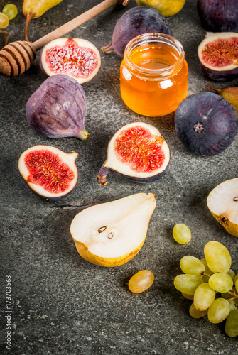 Snacks, dietary vegan desserts. Autumn fruits (figs, pears, grapes) with honey on a black stone table. Copy space