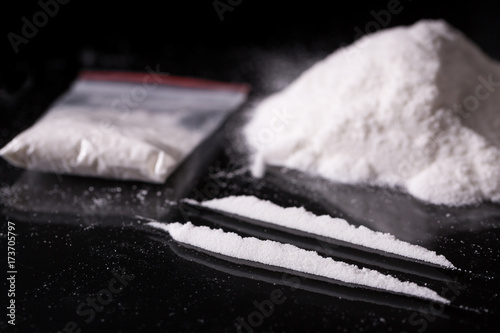 Plastic packet, two lines and pile of cocaine on black background