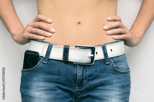 Waistline of woman body. Girl holding hands on waist close up..Sport, gym, diet. Mobile phone in jeans pocket close up.