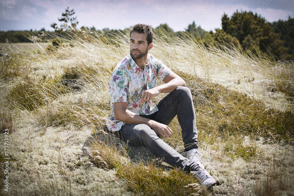 Handsome guy in floral shirt sitting in meadow