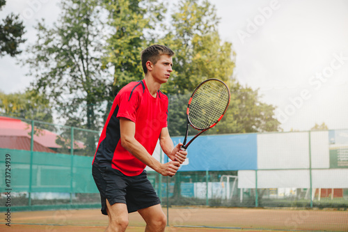 Handsome man in shirt holding tennis racket and looking concentrated while standing on tennis court © Ксения Левашова