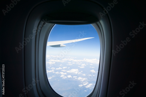 Outlook through plane window while traveling with window surround framing blue sky and clouds with focus on wing outside. © Brian Scantlebury