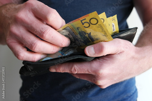 A man pulling out cash from wallet and counting fifty Australian dollar bills cash on hand to ready to pay, buy, or invest. photo