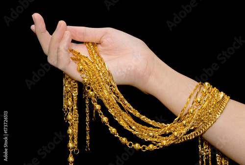 Woman hand holding expensive golden chains on black background