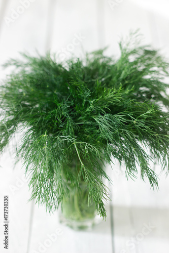 Fresh dill in a glass on a white wooden background. Rustic style, selective focus.