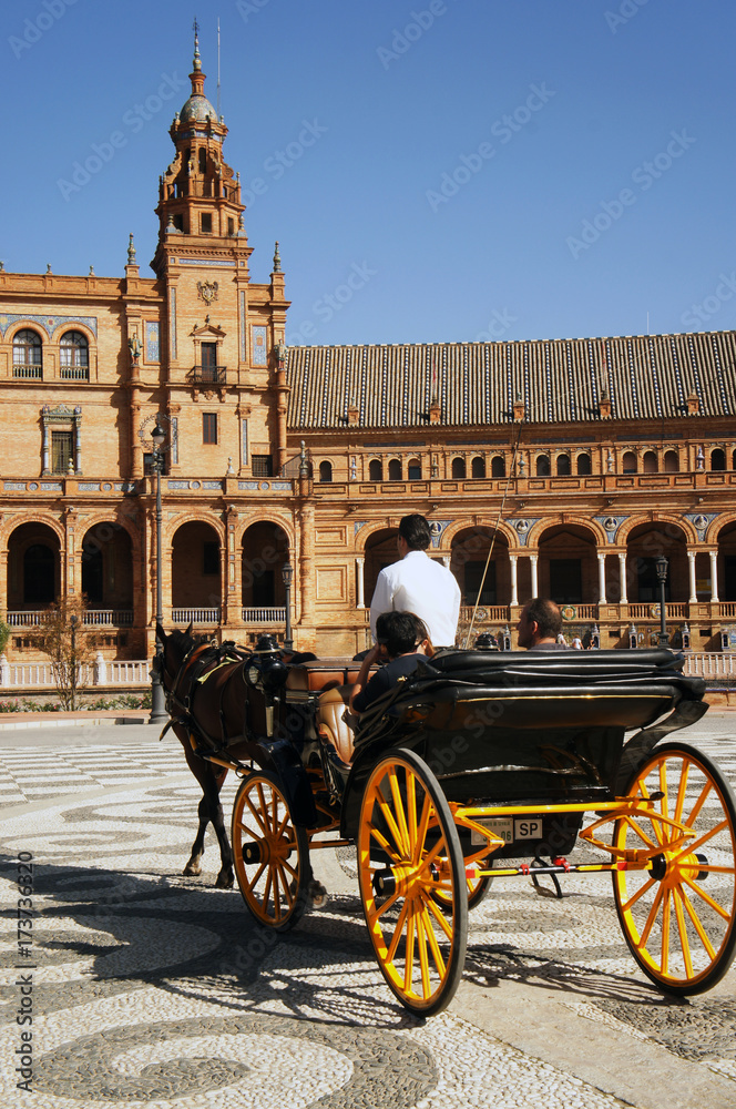 Carriage with yellow wheels with turists in front of the palace on Spain Square (Plaza de Espana) in Seville (Sevilla), Spain. Example of Moorish and Renaissance revival.