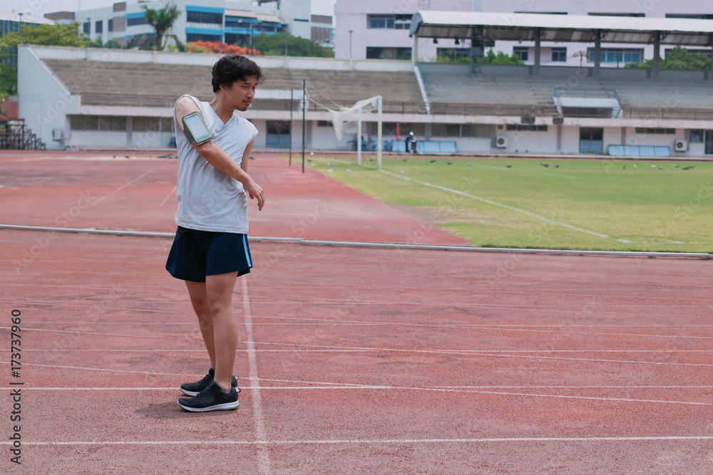 Portrait of handsome young Asian runner man warming up before run on track in the stadium with copy space background.