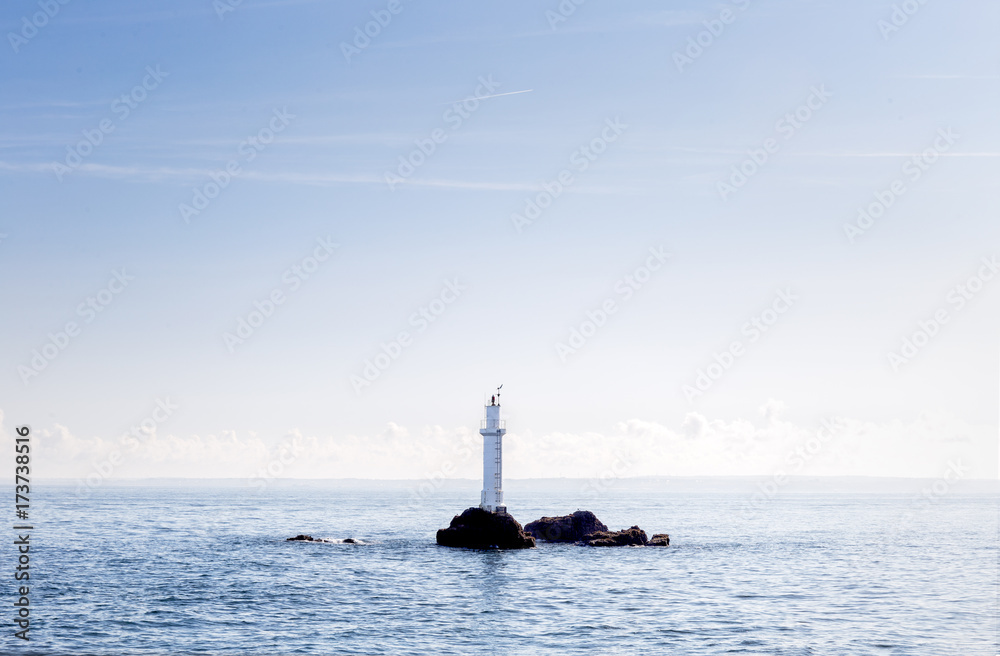 Lighthouse in the middle of the ocean with a blue and hazy sky