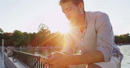Man sms texting using app on smart phone at sunset in city park. Handsome young business man using smartphone smiling wearing shirt outdoors in el Retiro in Madrid, Spain, Europe. Urban professional.