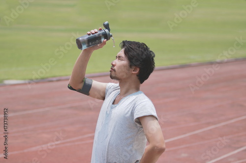 Fototapeta Naklejka Na Ścianę i Meble -  Healthy young Asian fitness man splashing water on his face after run in track of stadium.