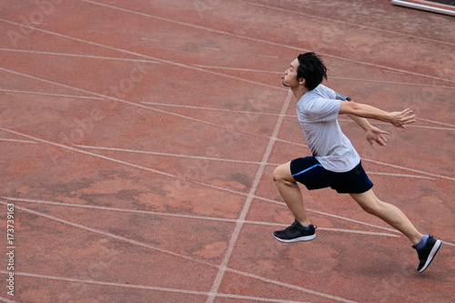 Athletic handsome young Asian runner sprinter crossing the finish line on track in stadium.