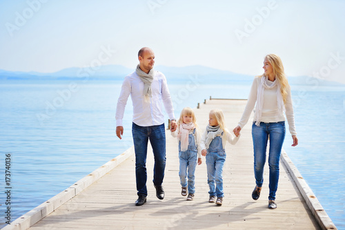 A young, friendly family: father, mother and two daughters are walking along the sea pier on a warm autumn day and having fun. They are happy.
