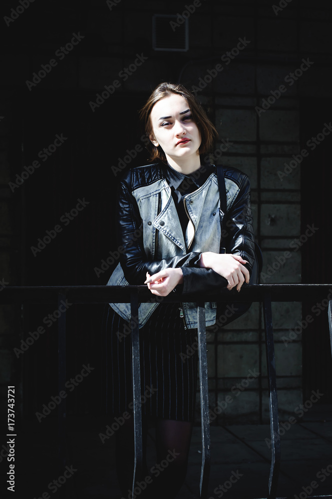 Naklejka premium street portrait of a girl student, fashionably dressed in dark clothes, with a black backpack and denim jacket autumn sunny day