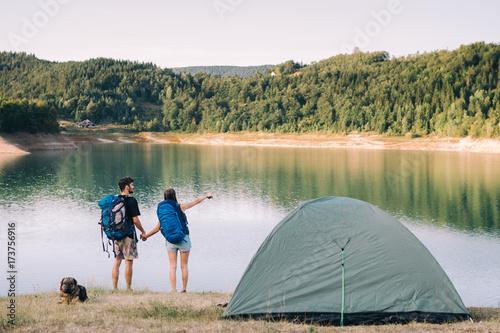 Hiking couple. Young couple with backpacks holding hands beside lake 