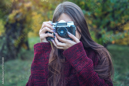 Beautiful woman in autumn Park holds vintage retro camera. Concept of photography as a hobby