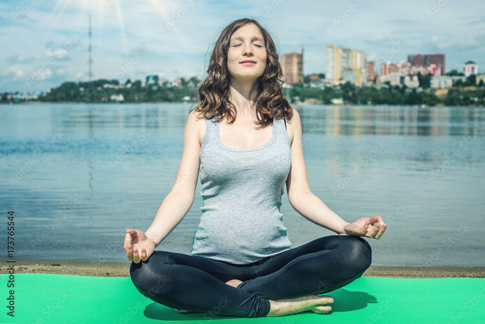 Pregnant woman doing yoga. Relaxation in the nature near the river.