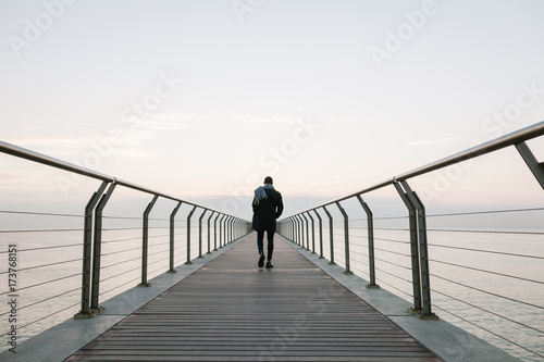Back view of man walking on bridge over sea photo