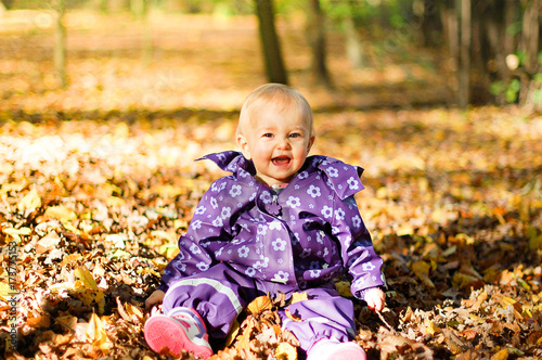 Baby sitting in the park surrounded by autumn leaves