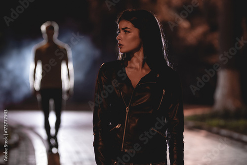 The scared woman stand on a dark street on a background of the man. night time