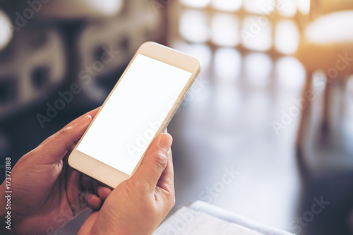Mockup image of hands holding and using mobile phone with blank white screen in modern cafe with blur bokeh background