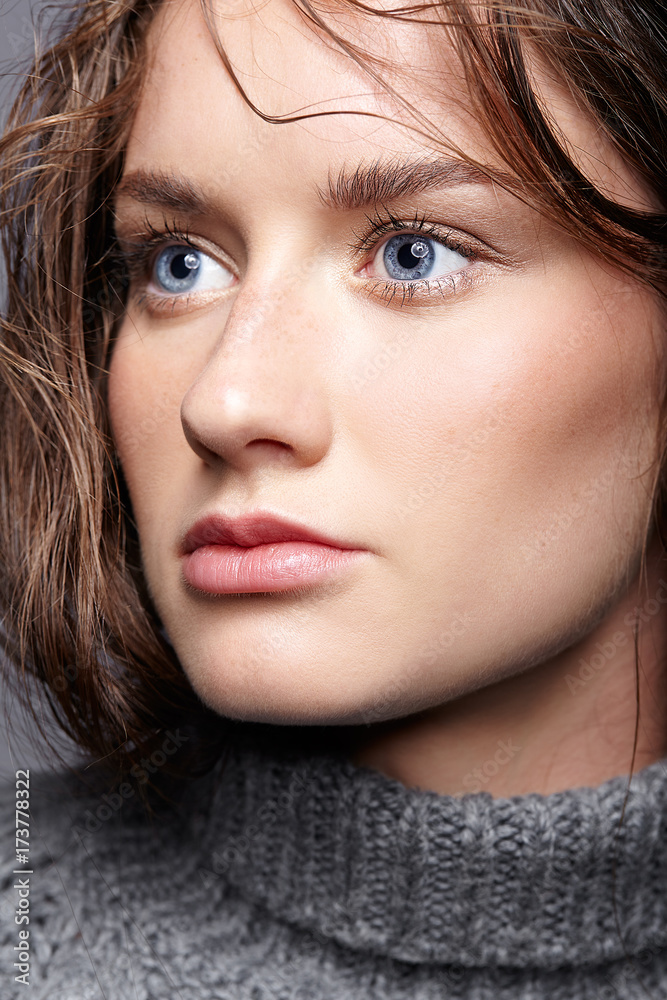 Fototapeta premium Beauty portrait of young woman in gray wool sweater. Brunette girl with bright blue eyes and day female makeup