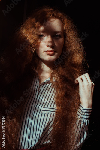 Pretty red haired model with freckles and long hair. Woman with shadow on her face