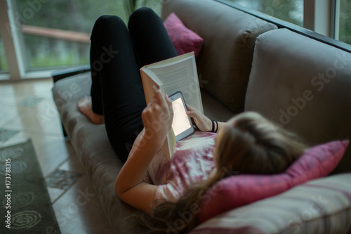 Teenage girl who is supposed to be reading with her cell phone behind the book