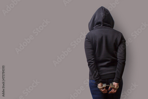 rear view of a girl in a black hood with handcuffed hands isolated on a gray background