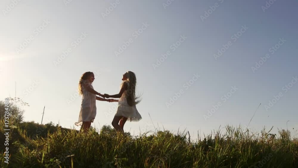 Two sisters in white dresses in the garden at sunset. The girls hug and laugh. Family relationships. Two sisters in white dresses in the garden at sunset. The girls hug and laugh. Family relationships.
