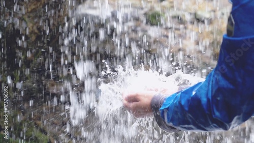 man refreshing his hands in stream of water of natural waterfall
