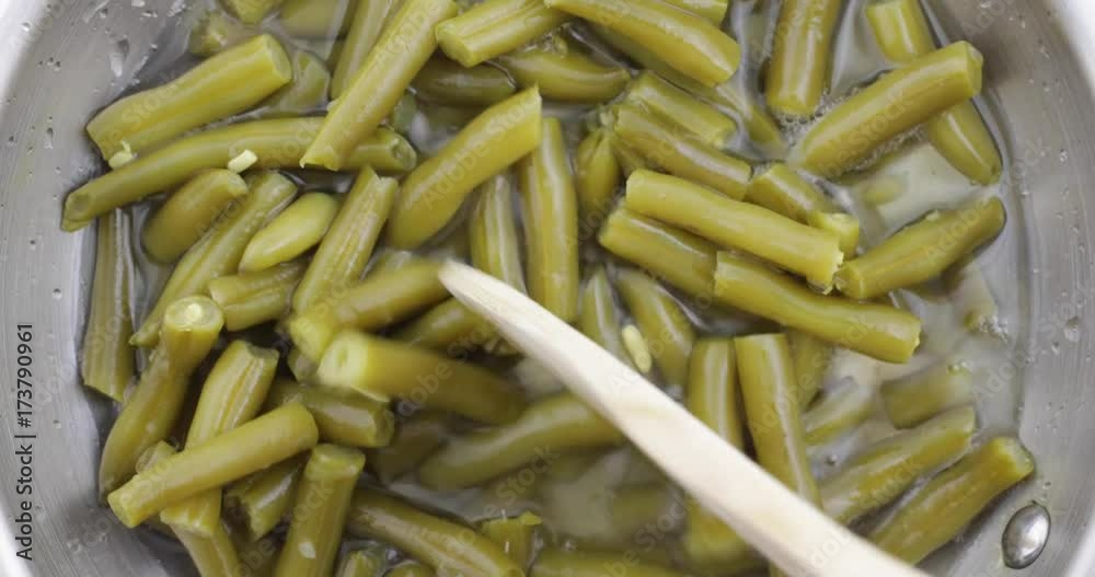 Top view of stirring green beans with a wood spoon in a pan while heating. Top view of stirring green beans with a wood spoon in a pan while heating.
