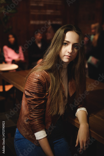street portrait of a female student in fashionable clothes  blue jeans and a brown jacket  in a cafe