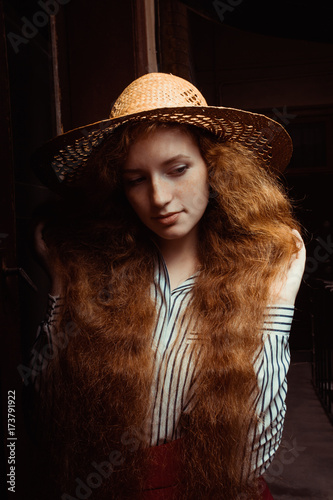 Attractive young red haired woman with freckles in straw hat posing in passage