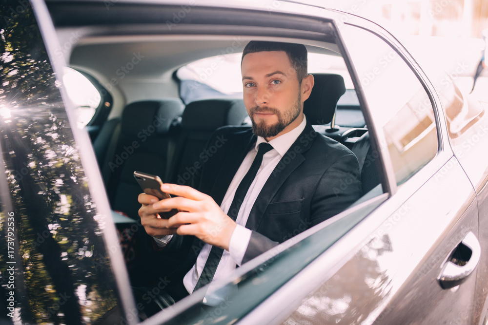 Businessman talking on the mobile phone and looking outside the window while sitting on back seat of car. Male business executive travelling by a car and making phone call.