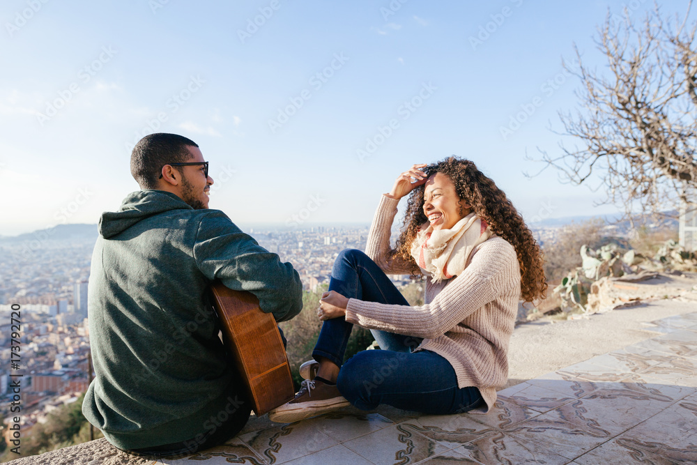 Man sitting playing guitar with his girlfriend above cityscape. Man sitting playing guitar with his girlfriend above cityscape.