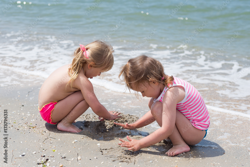 Children, little girls have fun playing with sand on the seashore in the summer. Children, little girls have fun playing with sand on the seashore in the summer.