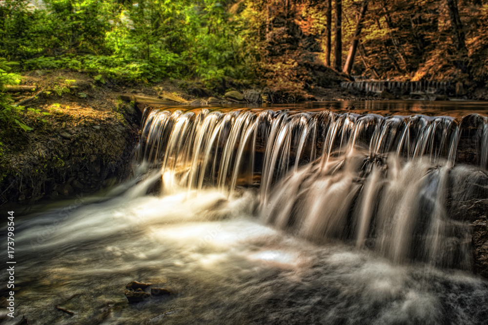 Obraz premium Waterfall in a forest. Abstract lanscape of moving nature from summer to autumn