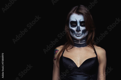 close up portrait of brown-haired woman with Halloween skull make up over black background.