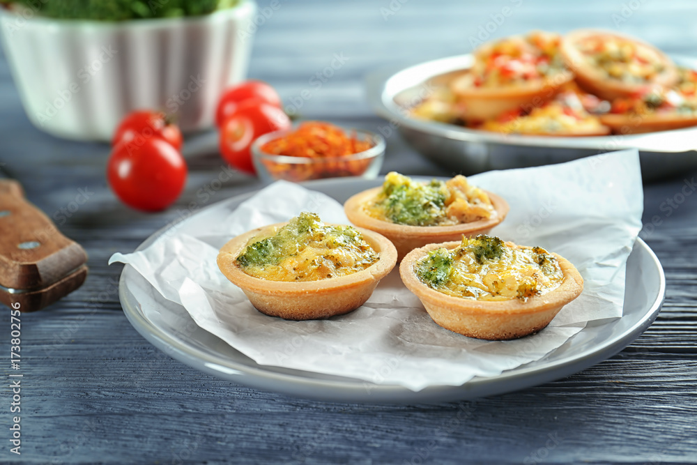 Plate with broccoli quiche tartlets on table