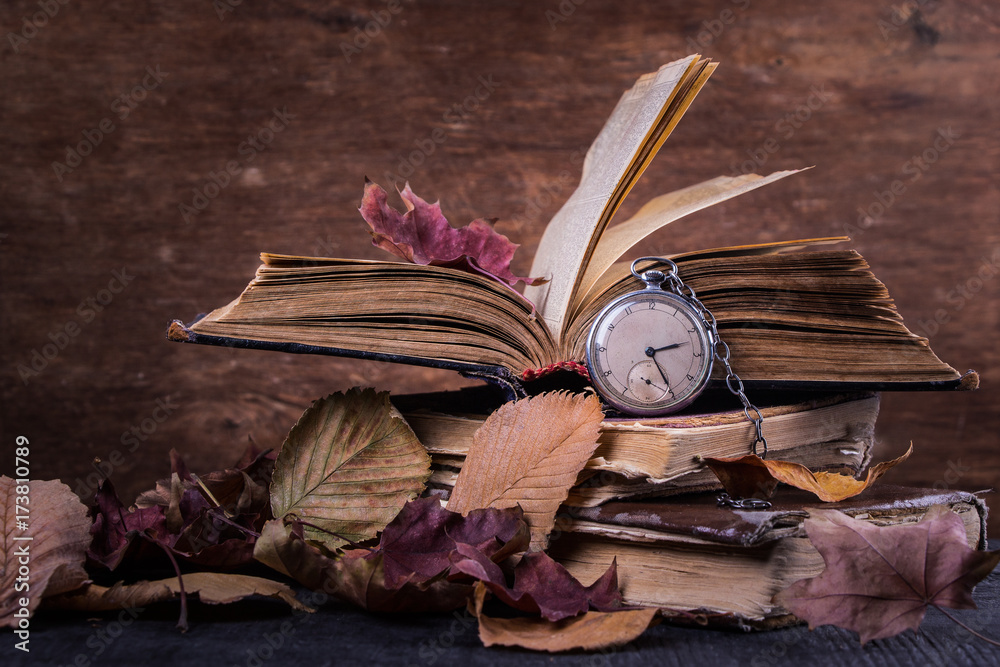 Obraz premium Decaying clock on the old shabby wise books with autumn dry yellow leaves on the dark wooden background
